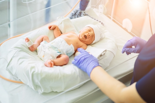 Picture of a female Nurse wearing gloves in a NICU and standing over a Newborn baby.