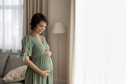 Picture of a smiling pregnant mother-to-be looking down at her belly as she holds it with two hands.