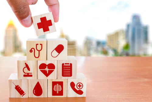 Picture of a person stacking blocks on one another in a pyramid shape. There is healthcare related icons on each block.