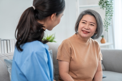 Picture of a middle aged woman sitting down on a couch while she talks to a female nurse. They are both smiling at each other.