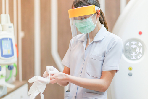 Picture of a female Nurse putting on gloves. She is wearing a face mask and face shield over her mask.