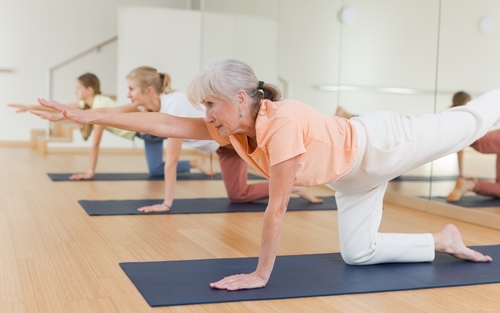 Picture of three females on mats doing some cardio exercise with one leg up in the air and one arm straight out in front of them.