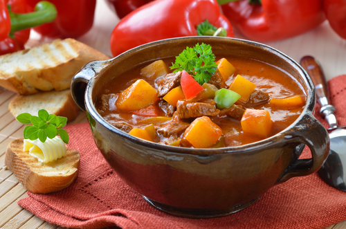 Picture of a bowl of tomato soup on a table with small pieces of garlic bread with butter on it.