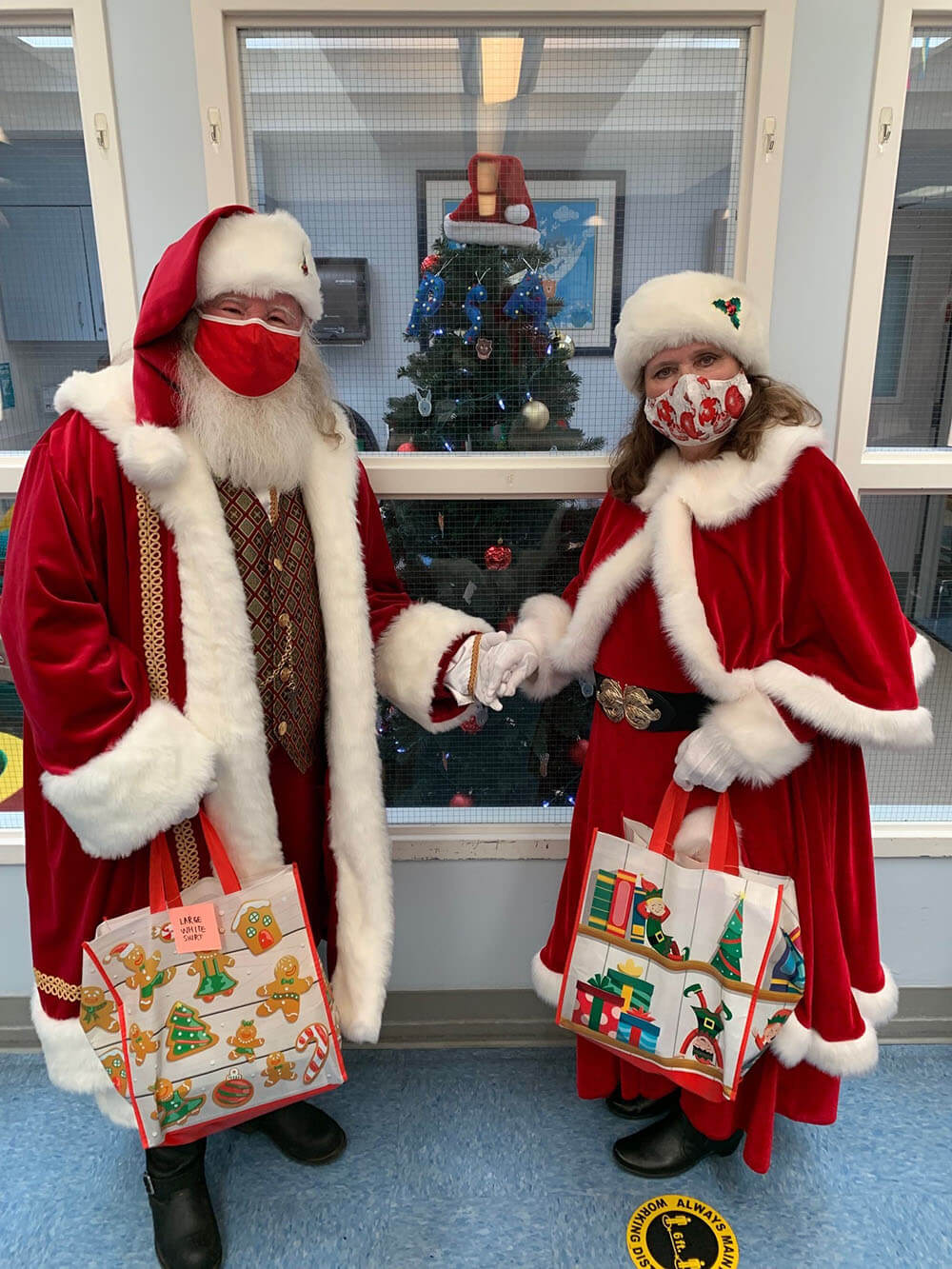 Santa and Mrs. Claus each holding a Christmas gift bag