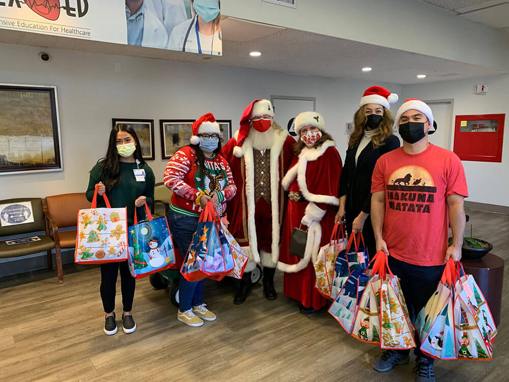 Santa, Mrs. Claus, and staff standing in the lobby holding bags of gifts for the children