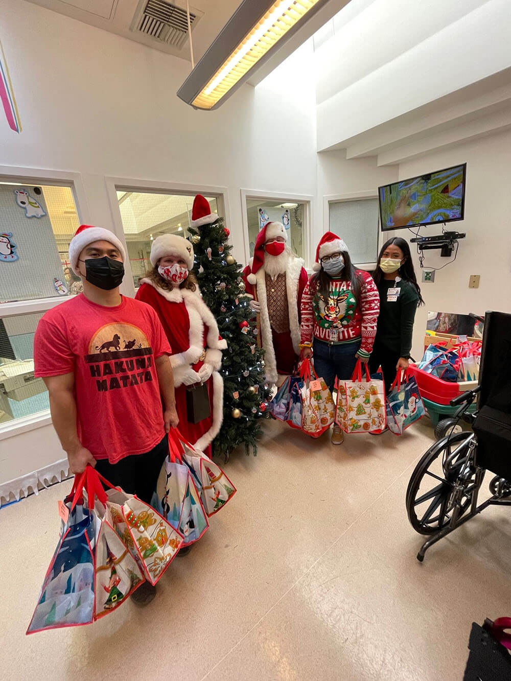 Santa, Mrs. Claus, and Staff standing in child play area and holding Christmas gift bags