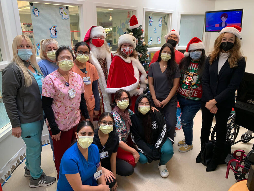 Santa, Mrs.Claus, and Staff standing in child play area and holding Christmas gift bags