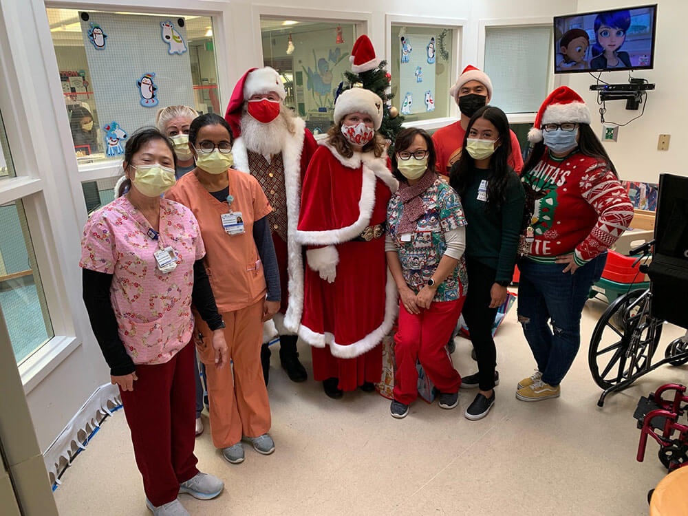 Santa, Mrs. Claus, and Staff standing in child play area and holding Christmas gift bags