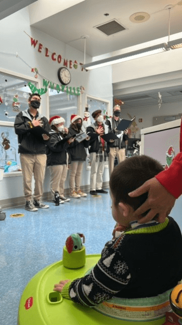 Cal High Christmas Carolers standing in front of children and adults in the Hospital, singing