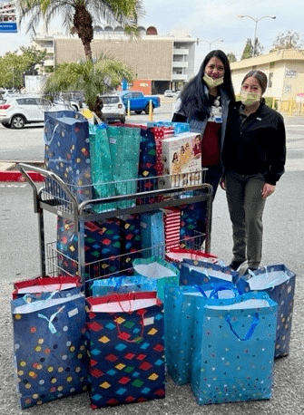 Two female Nurses standing outside with a cart full of Christmas gift Donations in gift bags